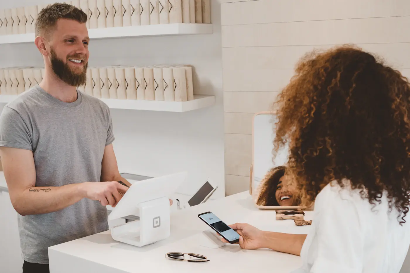 A shopkeeper serving a customer paying by phone at a card terminal