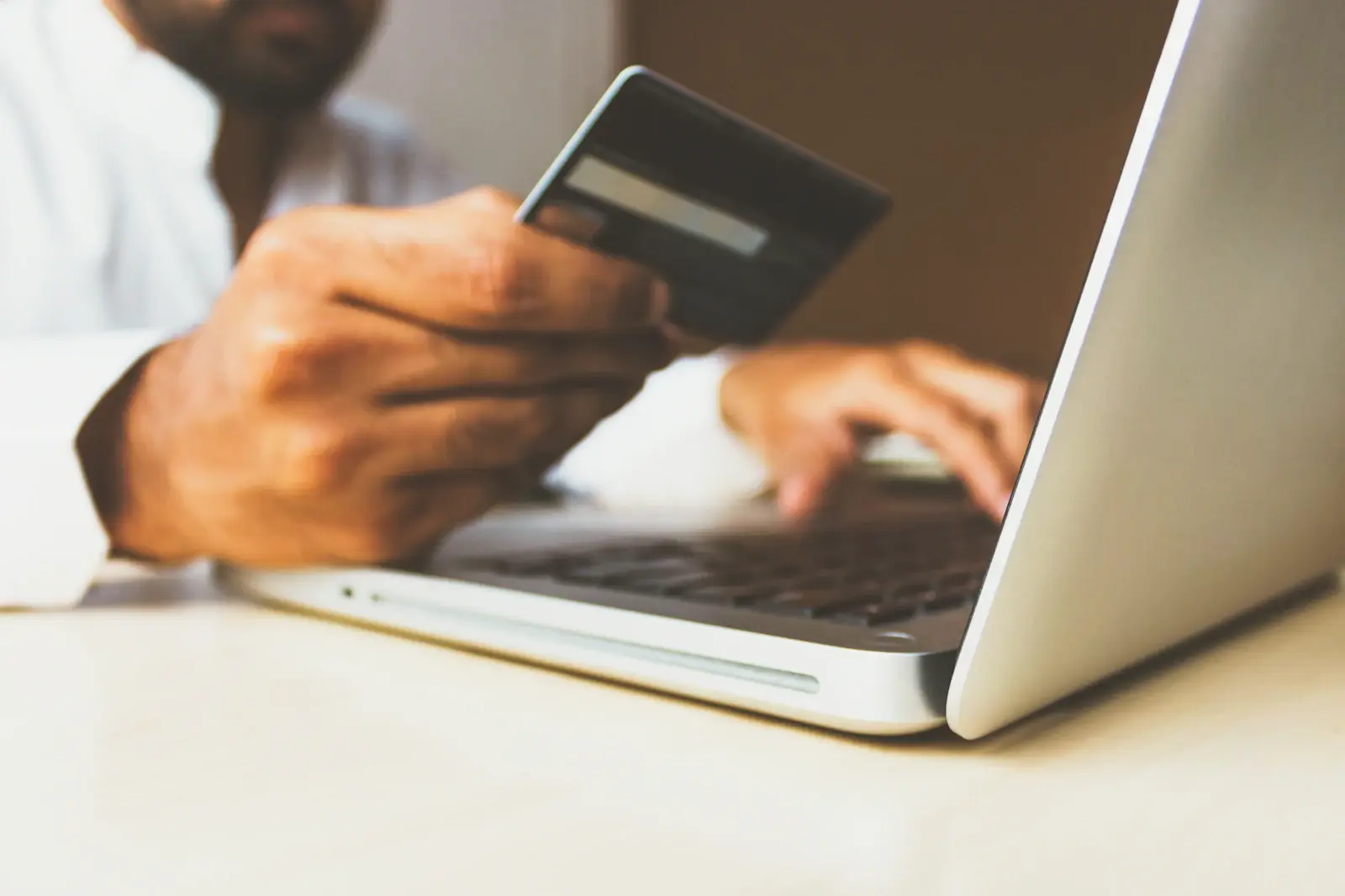 A person holding a payment card while typing on a laptop